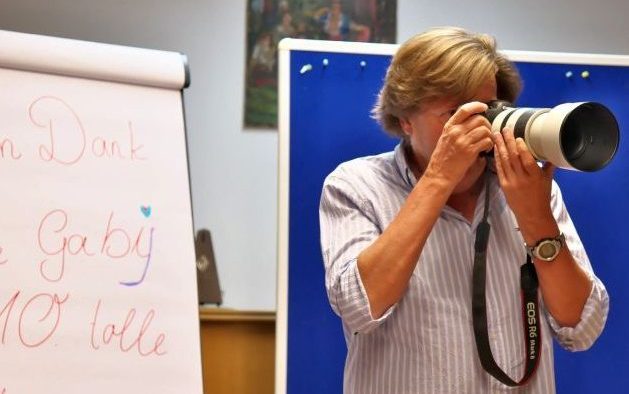 Ein Mann fotografiert mit einer großen Kamera in einem Raum mit einer Flipchart im Hintergrund.