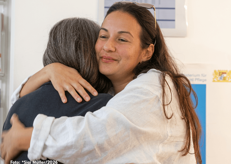 Zwei Frauen umarmen sich herzlich in einem hellen Raum.
