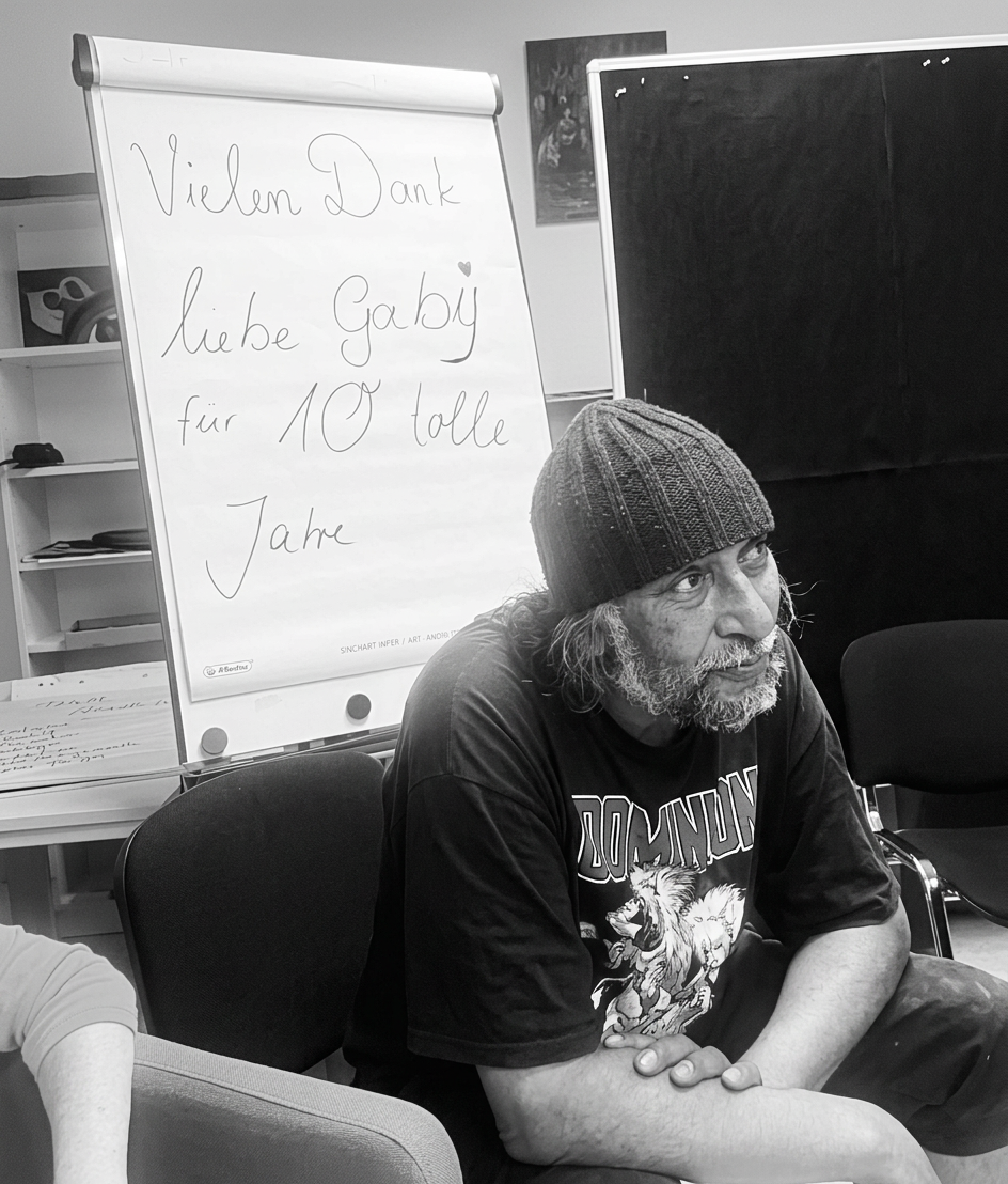 Ein Mann sitzt in einem Raum mit einem Flipchart im Hintergrund, auf dem steht: 'Vielen Dank liebe Gaby für 10 tolle Jahre'.