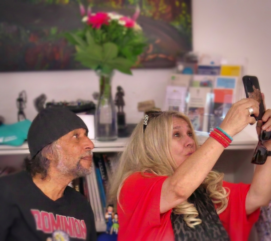 Ein älteres Paar posiert für ein Selfie in einem geschmackvoll eingerichteten Raum mit einem Blumenstrauß im Hintergrund.