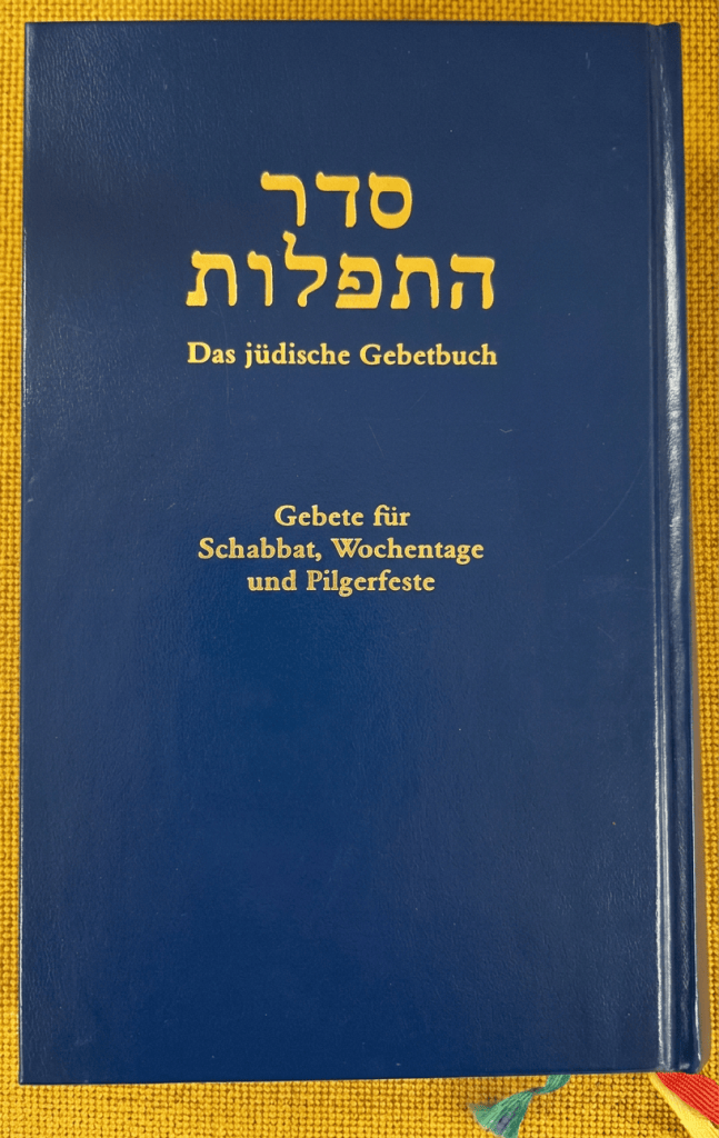 Ein jüdisches Gebetbuch in blauer Farbe, mit goldener Schrift auf der Vorderseite, das den Titel "Das jüdische Gebetbuch" trägt. Es enthält Gebete für Schabbat, Wochentage und Pilgerfeste.