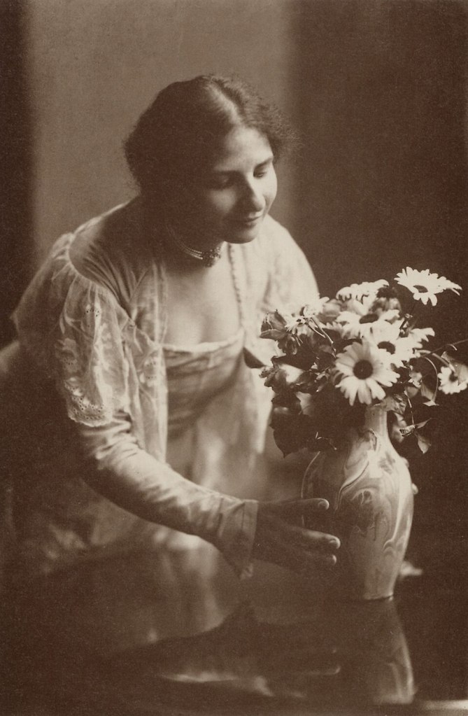 Eine Frau in vintage Kleidung betrachtet liebevoll einen Blumenvase mit Sonnenblumen und anderen Blumen.